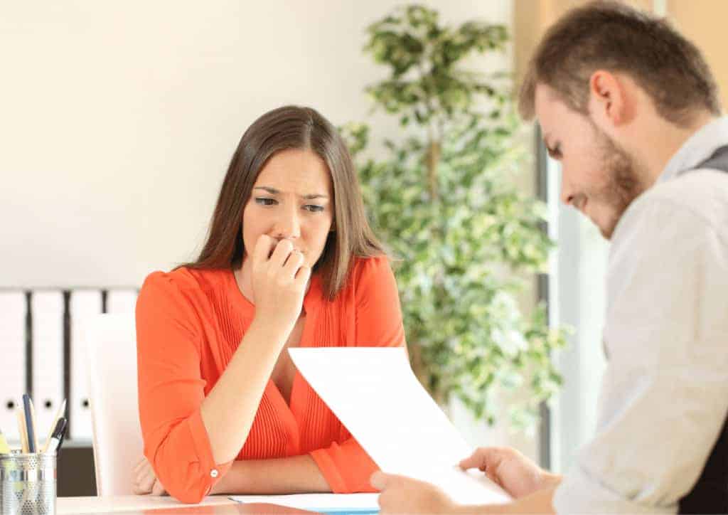 A young woman chews her nails whilst a manager reads through her resume