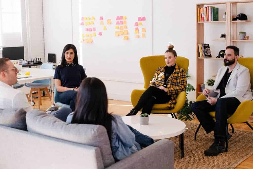 Five workers talk to one another in a casual work meeting