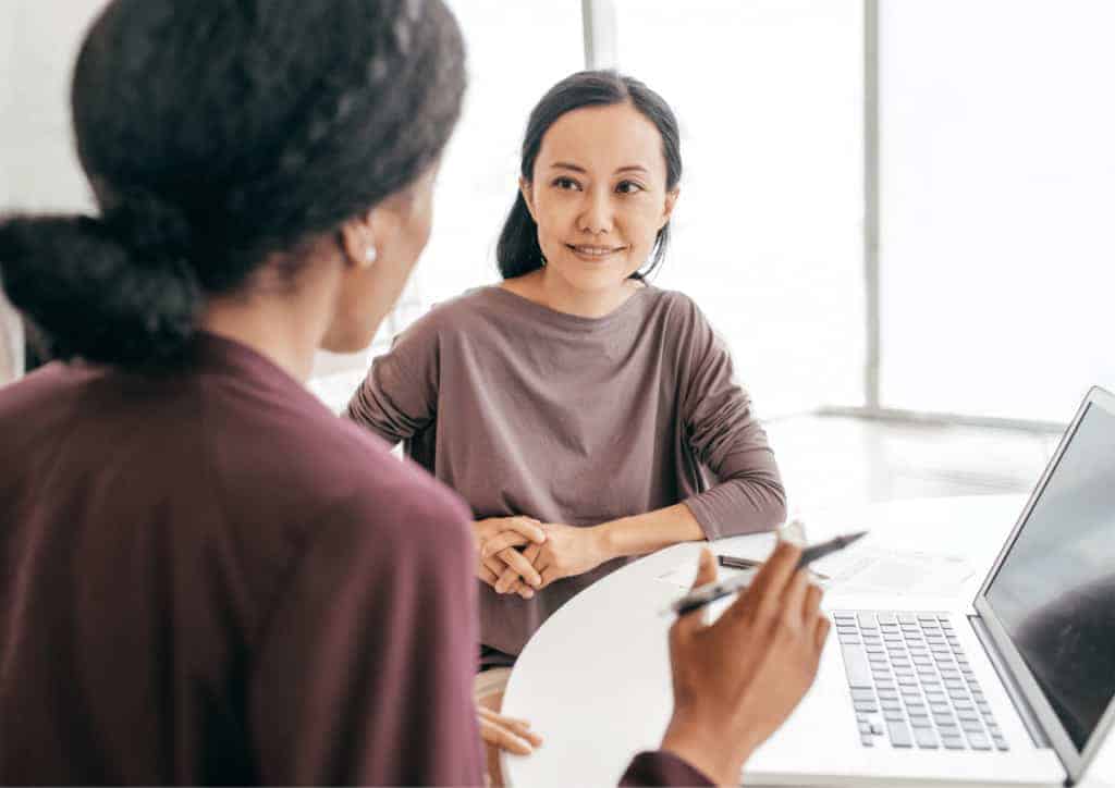 An interviewer talks to a smiling job applicant at a circular table